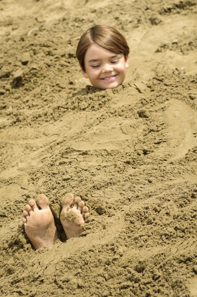 child buried in the sand at beach