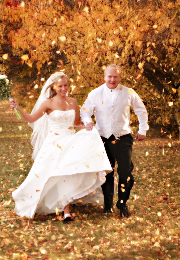 bride and groom running through fall leaves